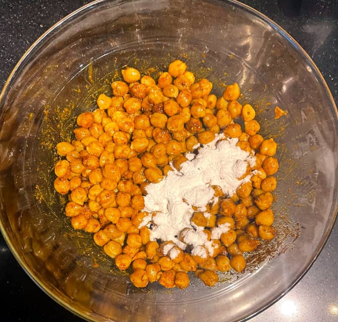 Rice flour added to chickpeas and spices in bowl.