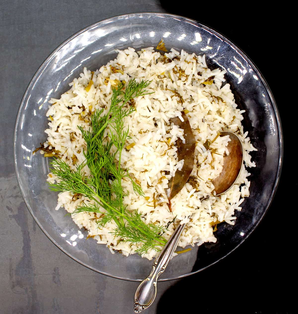 Dill rice in glass bowl with spoon and fresh fronds of dill.