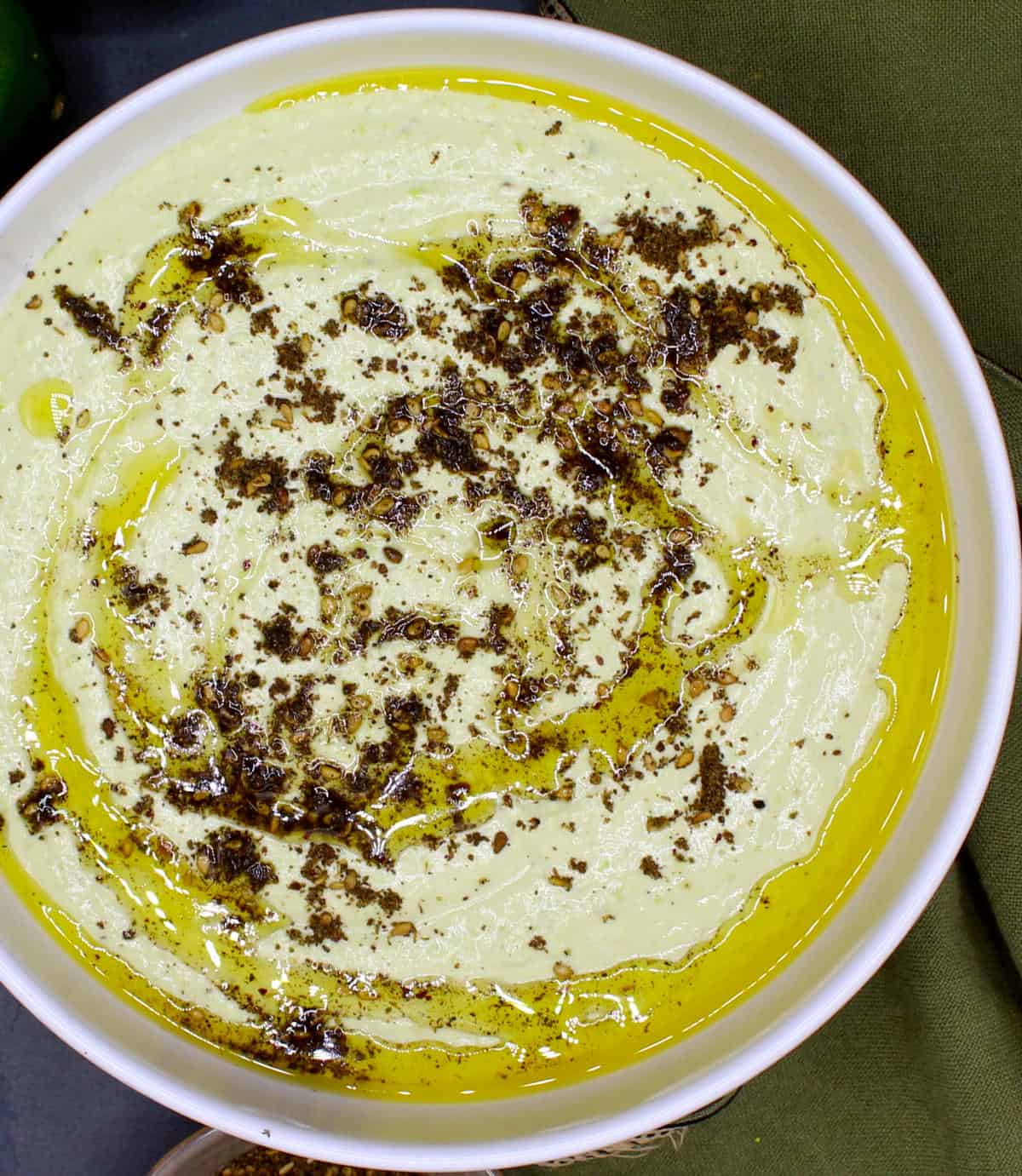 Hummus de edamame en un tazón blanco con una pizca de za'atar y aceite de oliva.