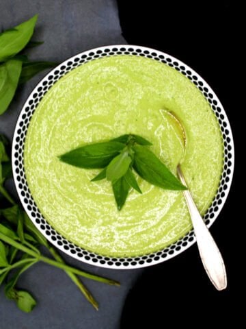 A bowl of mint chutney with mint leaves and a spoon.