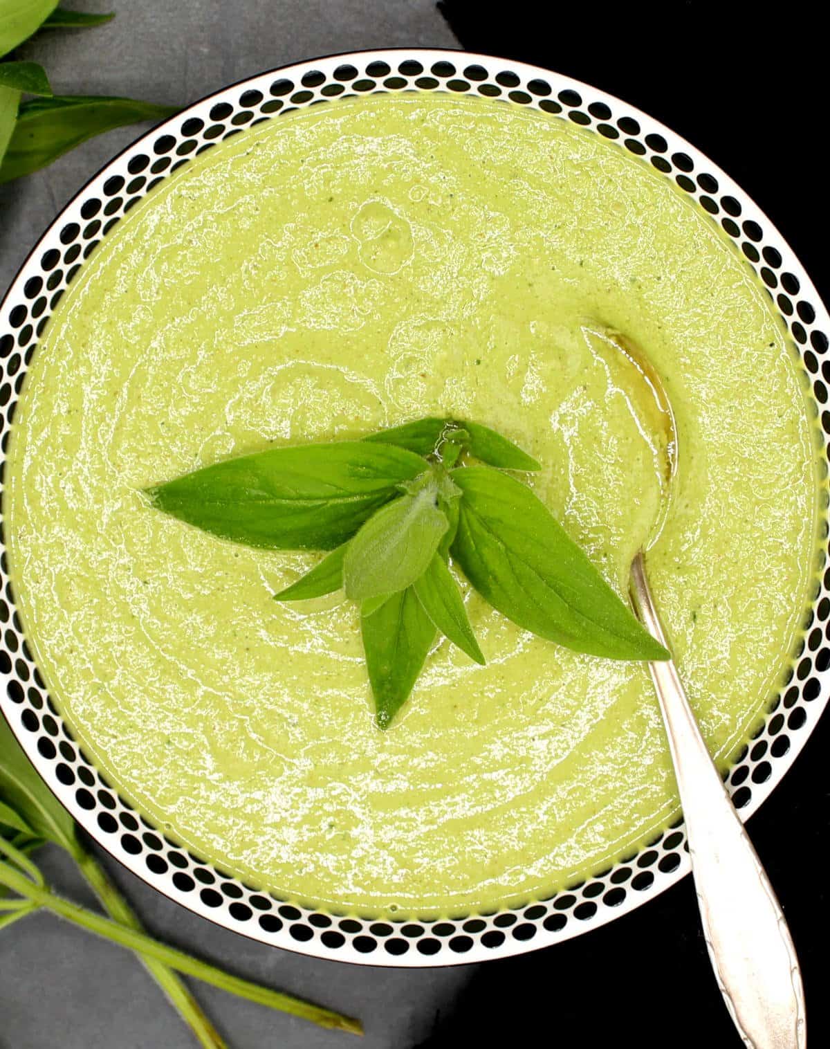 Mint chutney in a white bowl with black dots with a sprig of mint and a spoon.