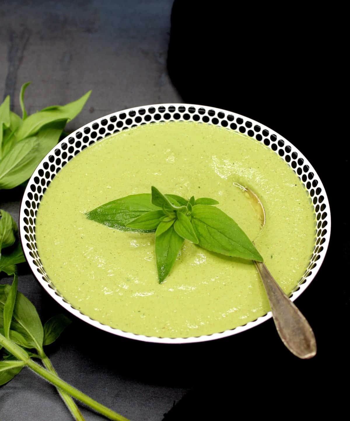 Mint cilantro chutney in a white bowl with black dots with sprigs on mint and a spoon.
