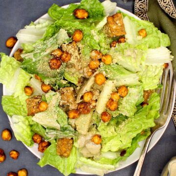 A plate of vegan caesar salad with dressing, chickpeas, tempeh and vegan parmesan cheese.