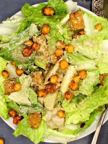 A plate of vegan caesar salad with dressing, chickpeas, tempeh and vegan parmesan cheese.