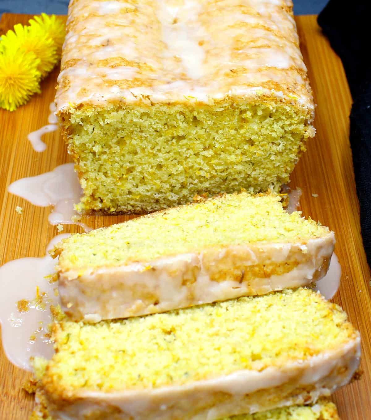 Sliced dandelion bread with lemon glaze on cutting board with the tender, cake-like crumb showing.