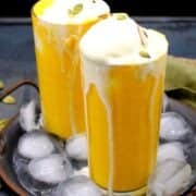 Image of two tall glasses of mango smoothie topped with ice cream with text inlay that says "vegan mango smoothie, five minutes, five ingredient recipe"