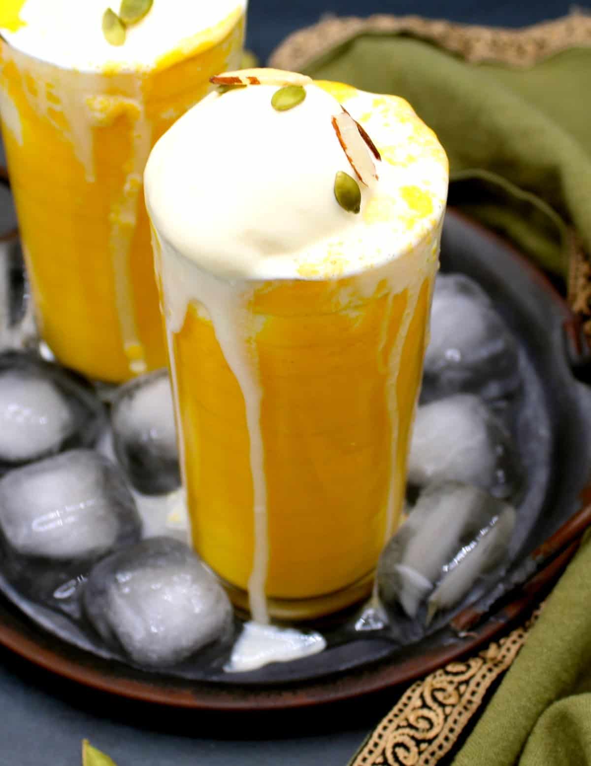 Glasses of vegan mango smoothie with ice cream in an ice-filled tray. A green napkin is around it.
