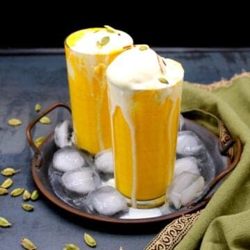 Tall glasses of vegan mango smoothie topped with ice cream in a copper tray with ice cubes.
