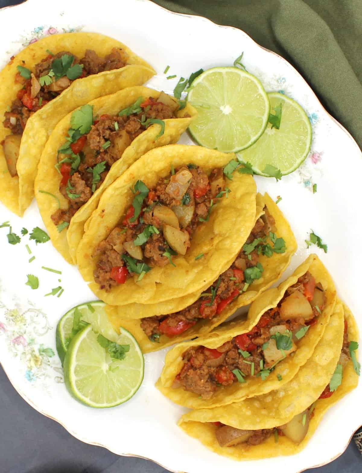 Veganistische picadillo-taco's op een witte schotel met schijfjes limoen.
