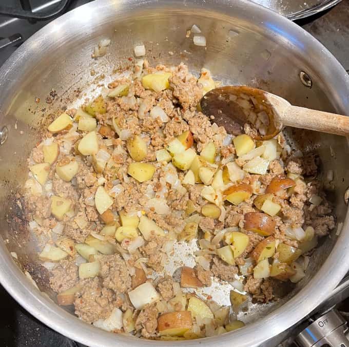 Potatoes added to vegan meat in skillet.
