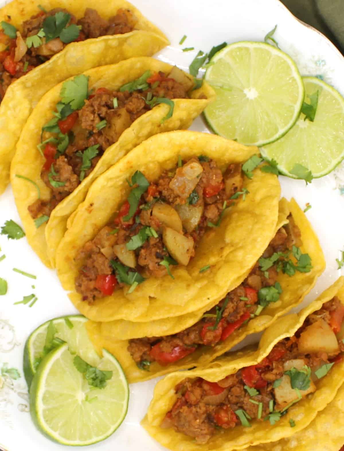 Picadillo tacos on white platter with lime slices.