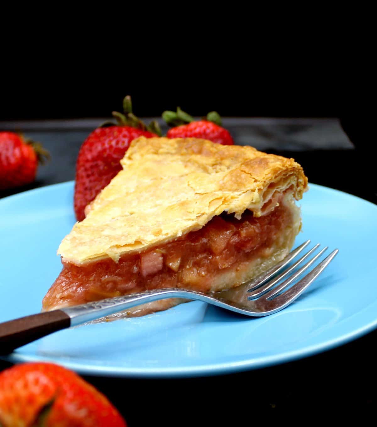 A slice of vegan pithivier with the rhubarb strawberry filling showing and a fork. On the side are more strawberries.