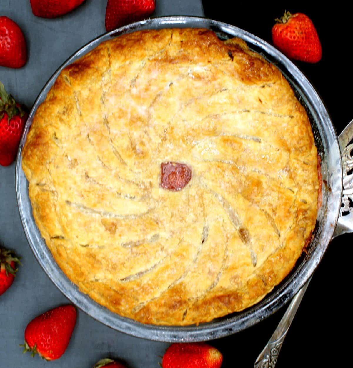 A vegan strawberry rhubarb pithivier in pie plate with strawberries scattered around.