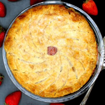 Strawberry rhubarb pithivier in a glass pie plate surrounded by fresh strawberries.