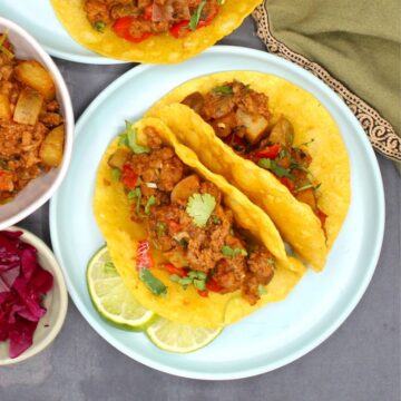 Veganistische picadillo-taco's in een blauw bord met meer vulling en rodekoolsnippers aan de zijkant.
