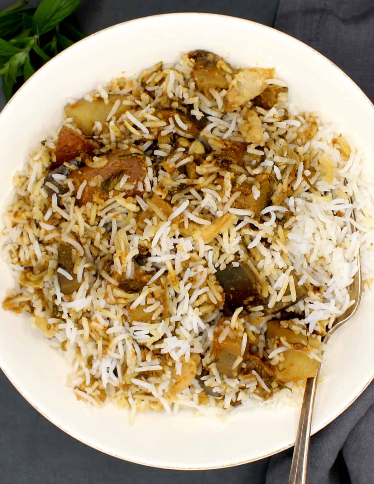 White bowl with eggplant biryani and a fork.