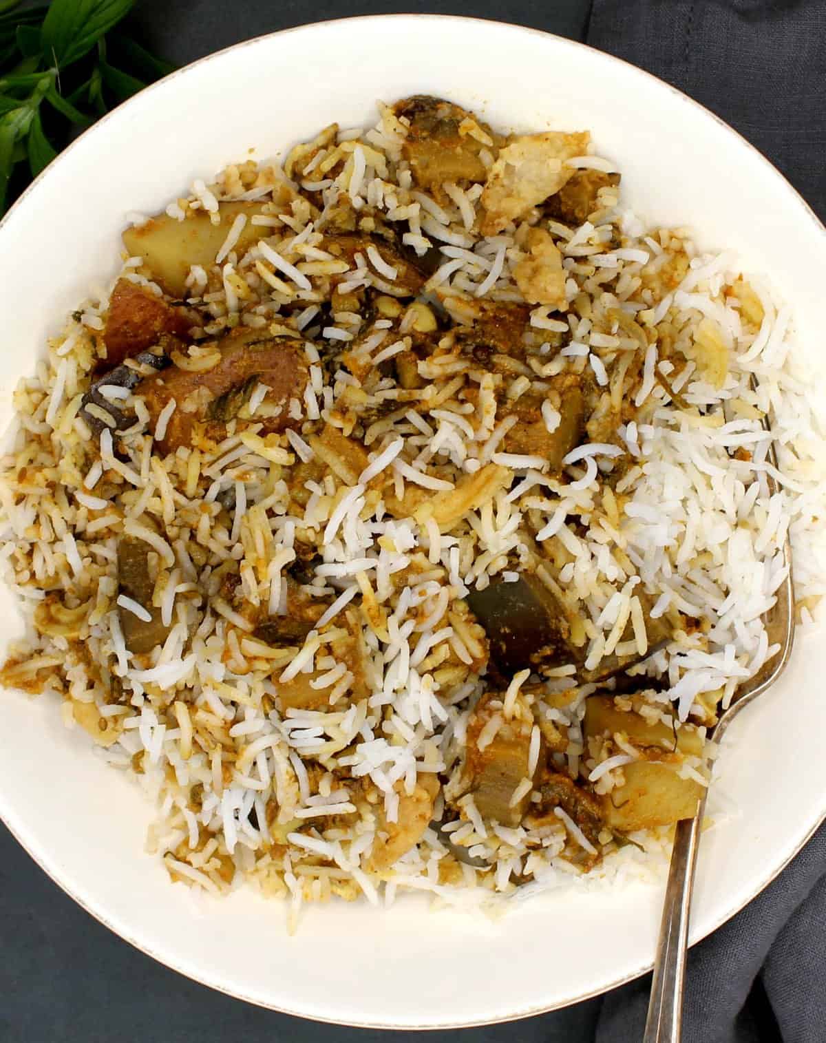 Eggplant biryani in a white bowl with chunks of eggplant, potatoes and a fork.