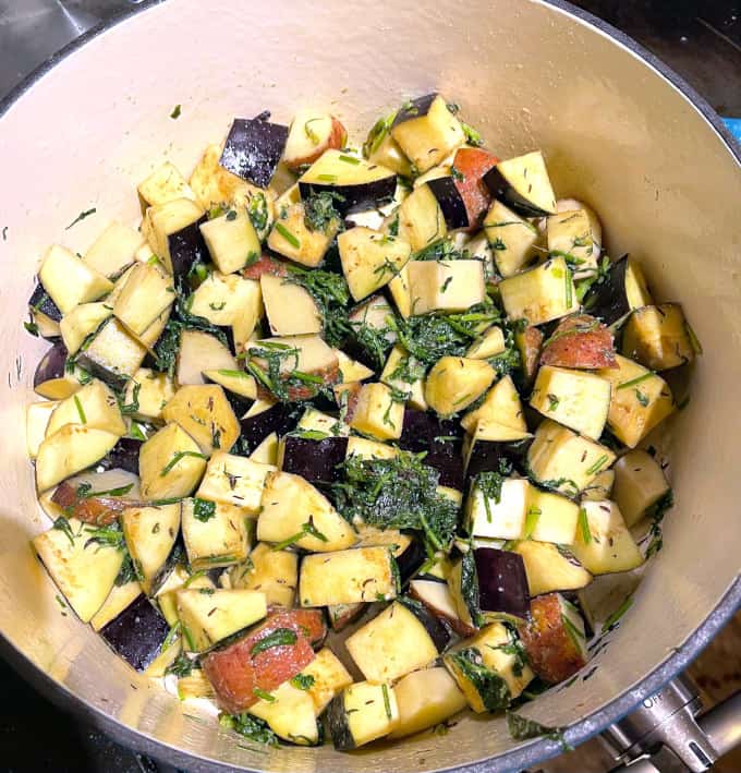 Eggplant and potato cubes in pot with herbs.