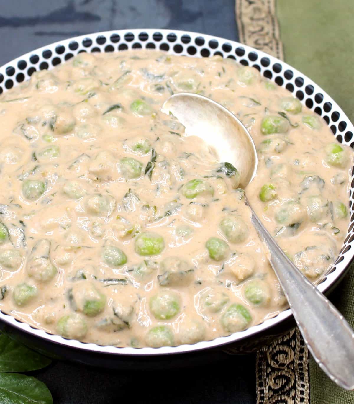 Methi matar malai in white and black bowl with silver spoon.