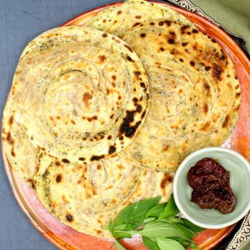 Pudina paratha in earthen plate with pickles and mint leaves.