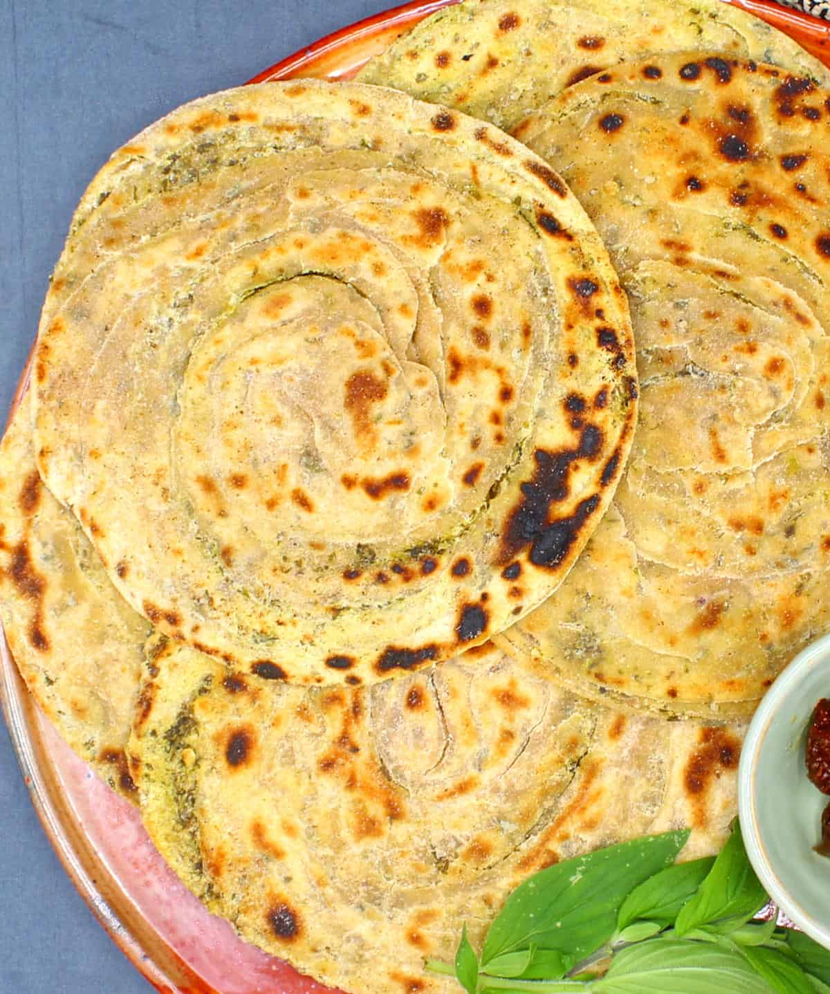 Pudina parathas on an earthen plate with pickles and mint leaves.