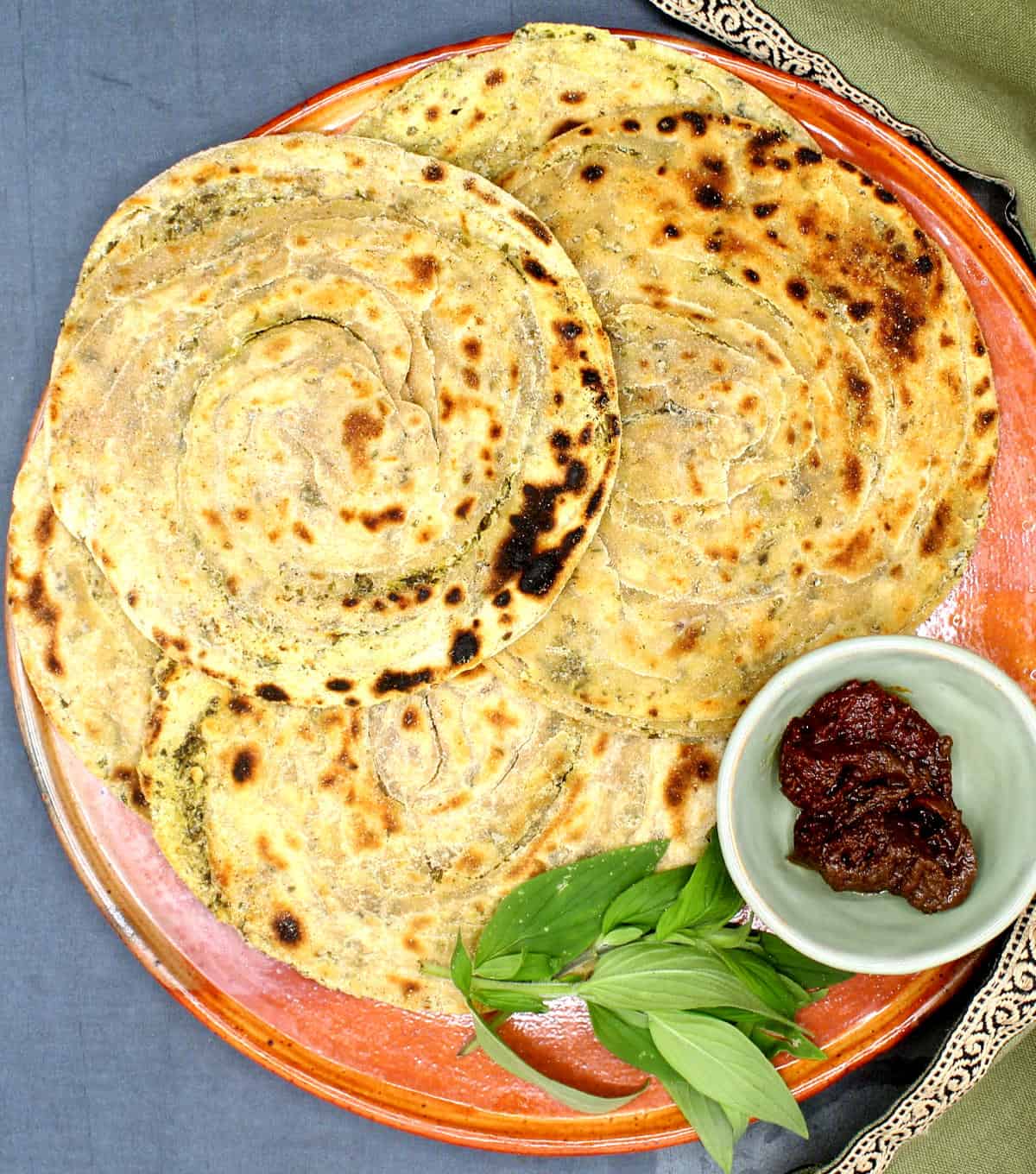 Pudina paratha on an earthen plate with pickles and mint leaves.