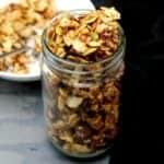 Vegan keto granola in a glass jar with a white bowl with granola and almond milk in background.