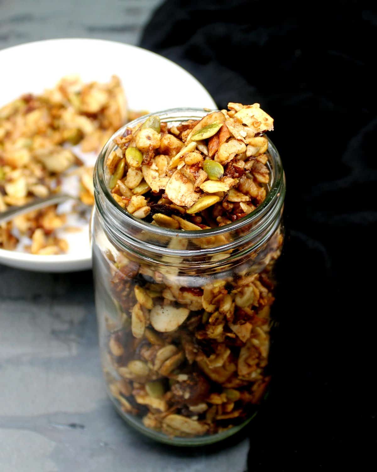 Vegan keto granola in glass jar. Behind it is a white bowl with granola and almond milk.