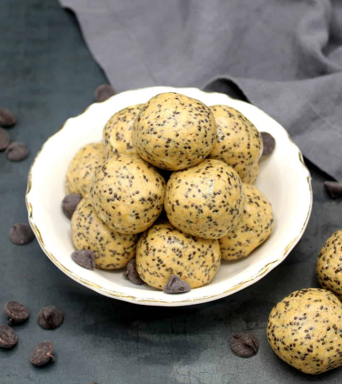 Veganska proteinenergibollar i vit skål med fler energibollar och chokladbitar utspridda.