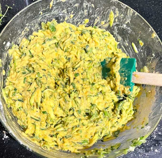 Zucchini fritter batter in mixing bowl with spatula.