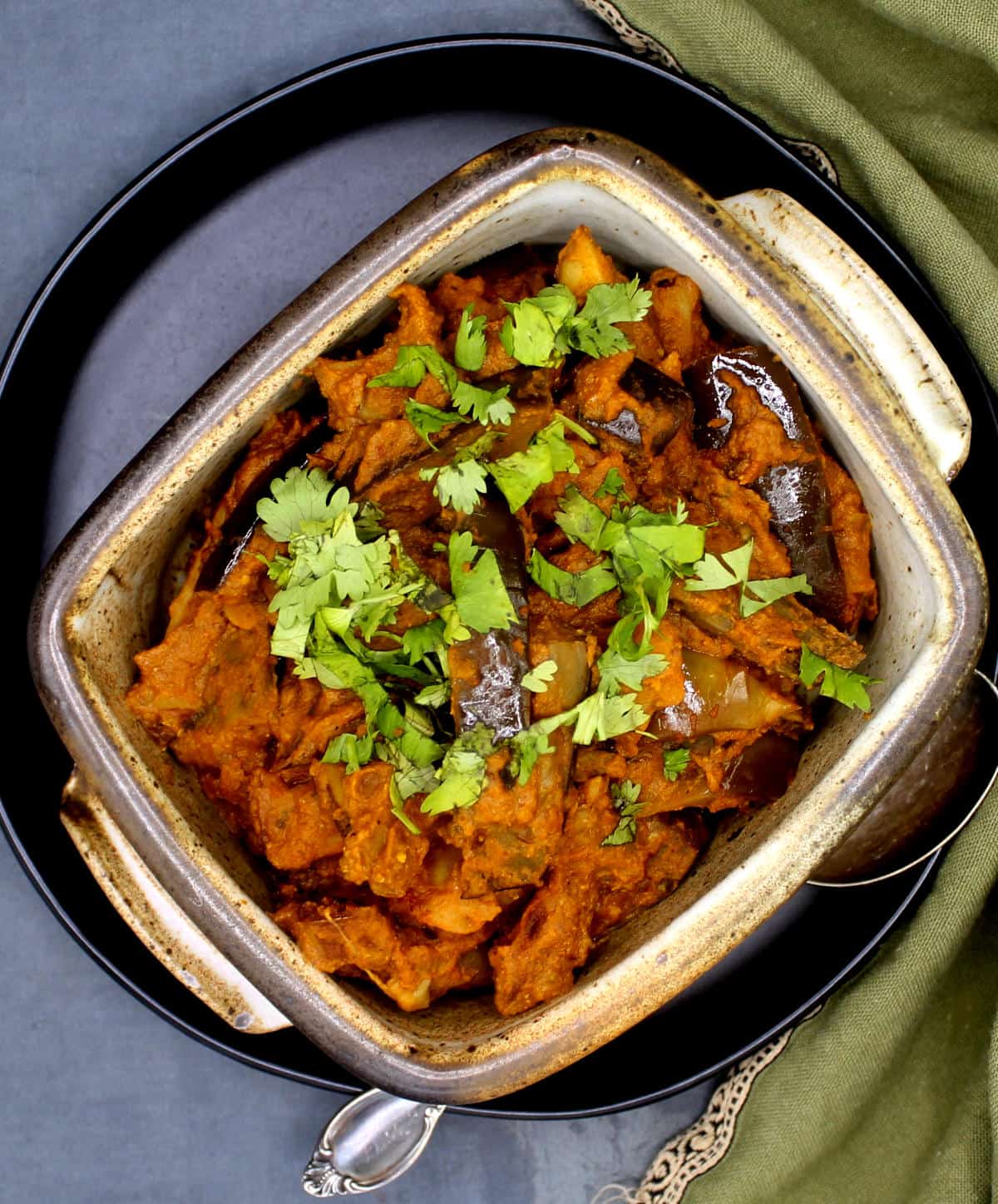 Baingan Masala or brinjal masala in clay bowl on black plate with cilantro garnish.
