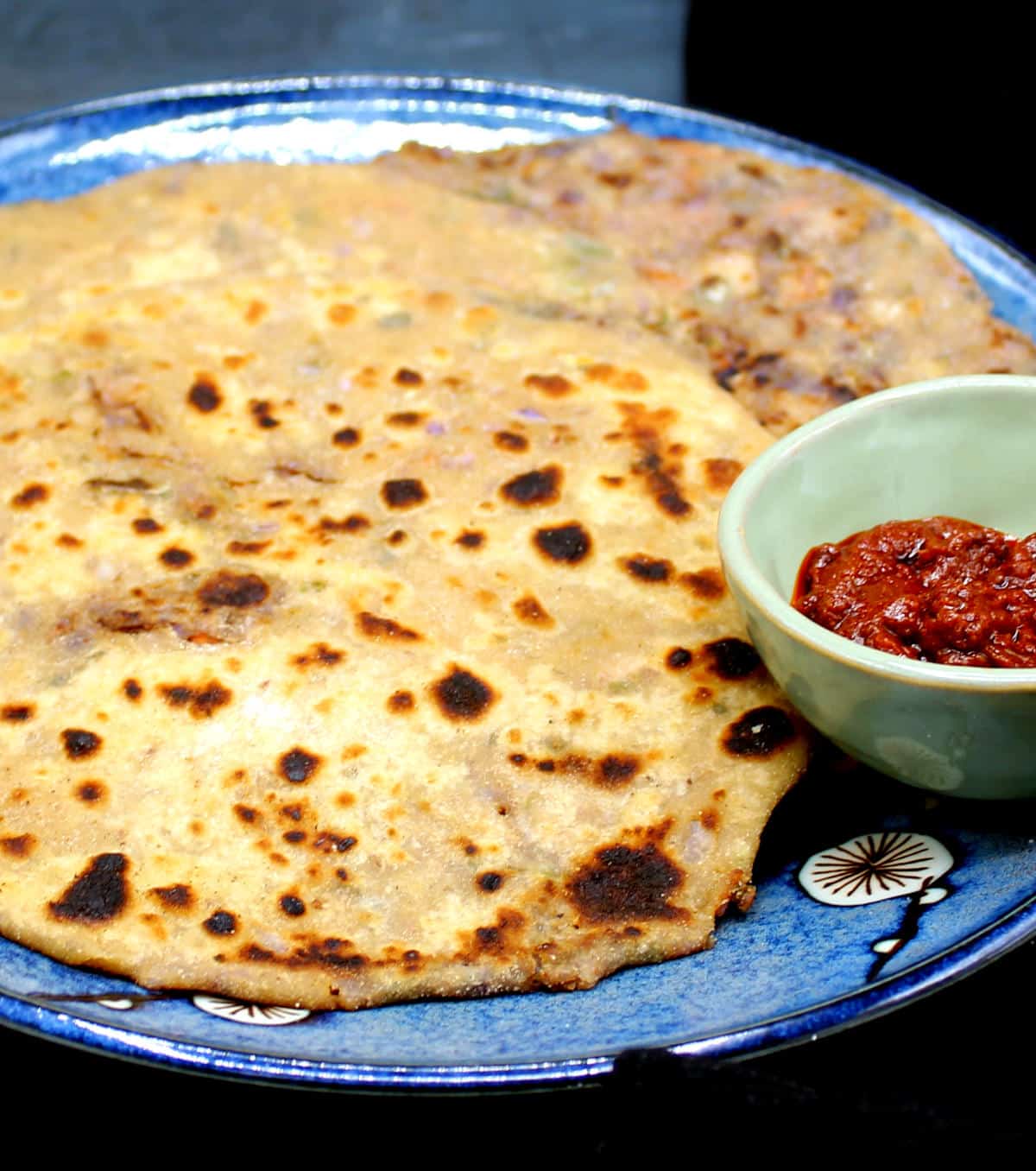 Parathas in a blue plate with spicy pickles in a bowl.