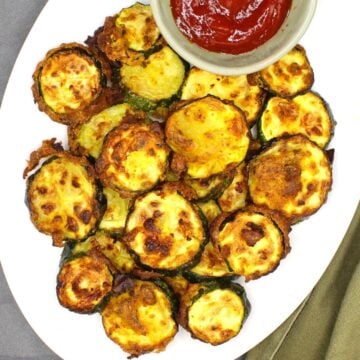 Air fryer zucchini chips in white plate with tomato ketchup.