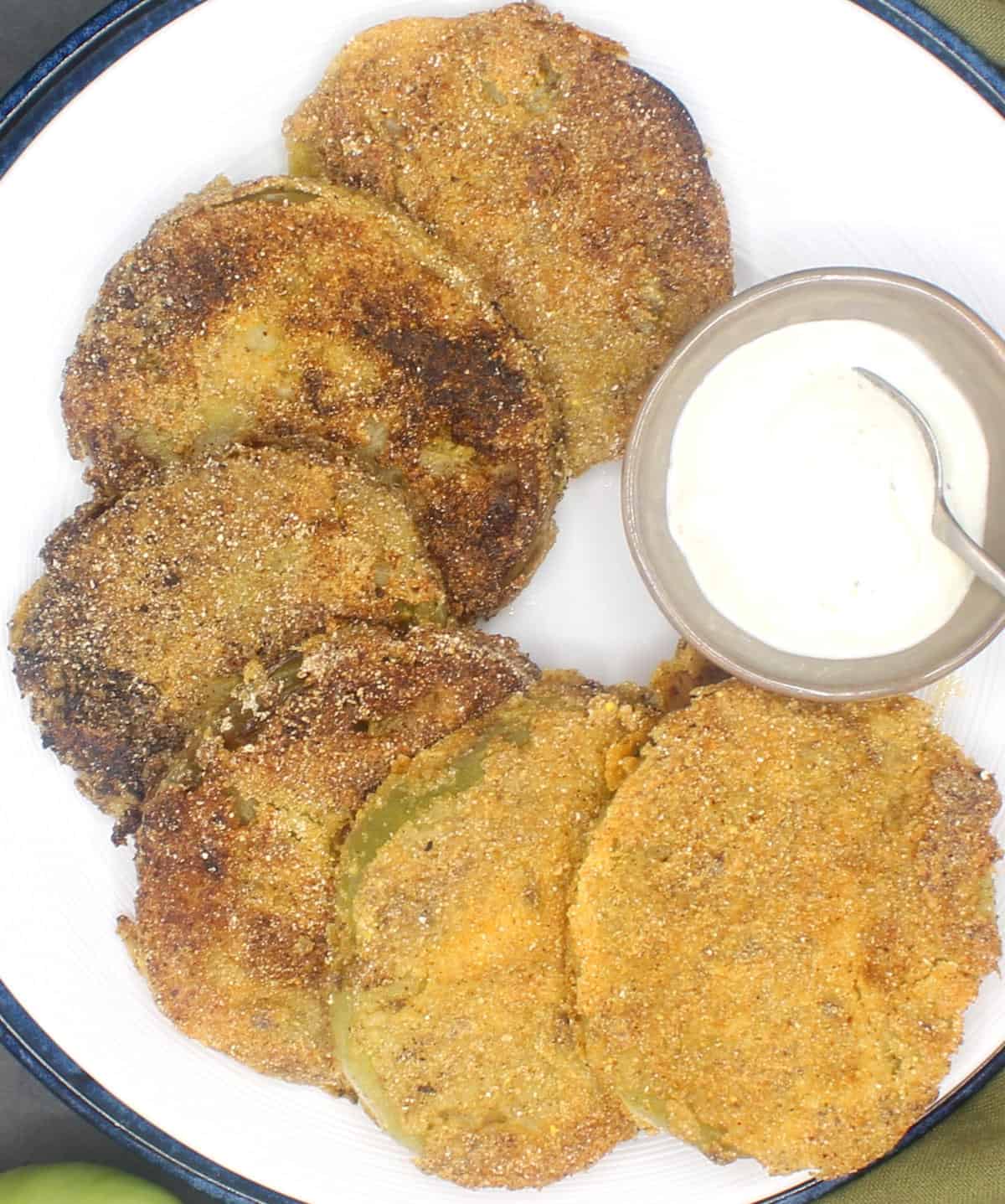 Slices of vegan fried green tomatoes on white plate with spicy mayo in small bowl.