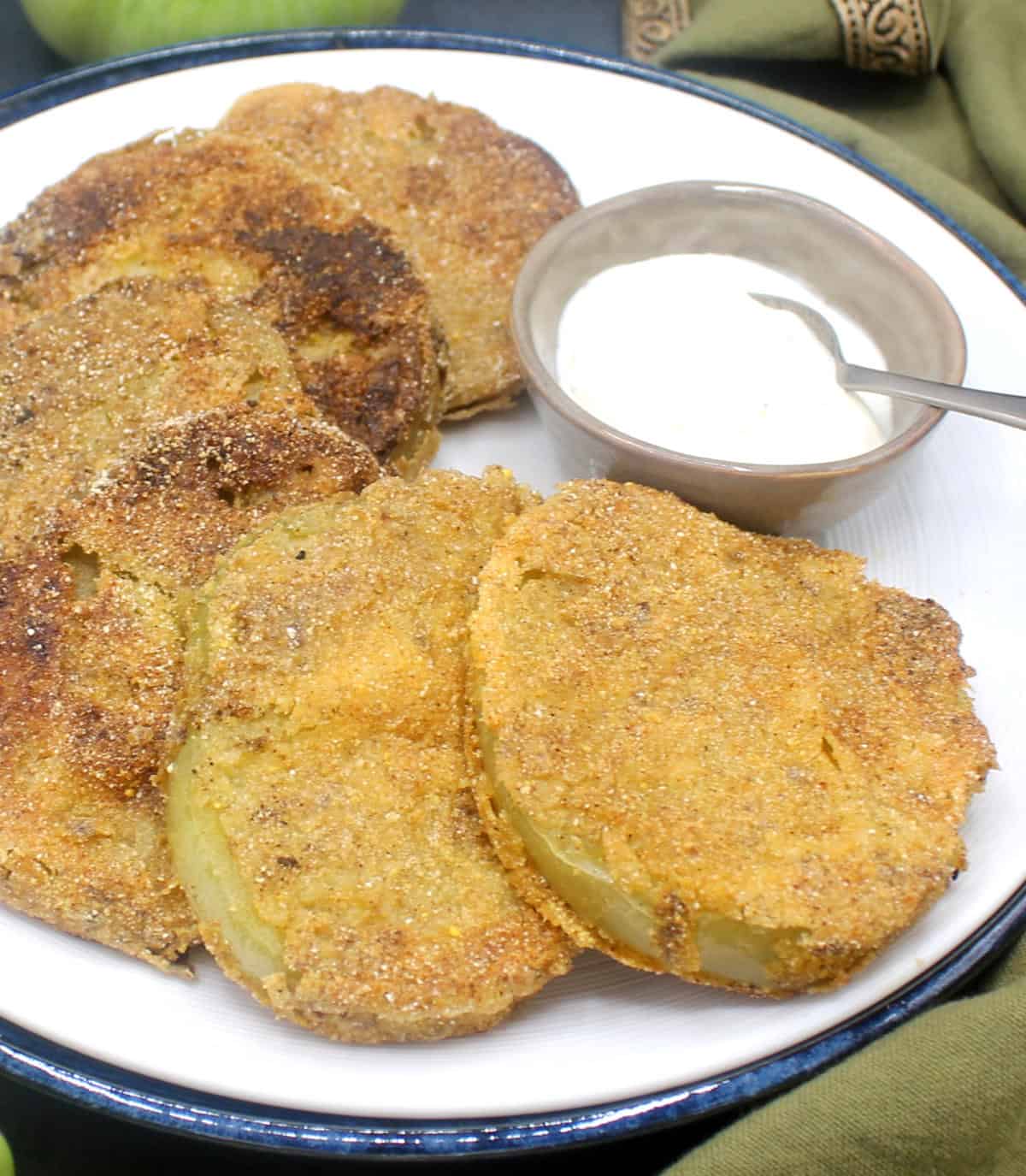Vegan fried green tomato slices on white plate with remoulade in bowl.