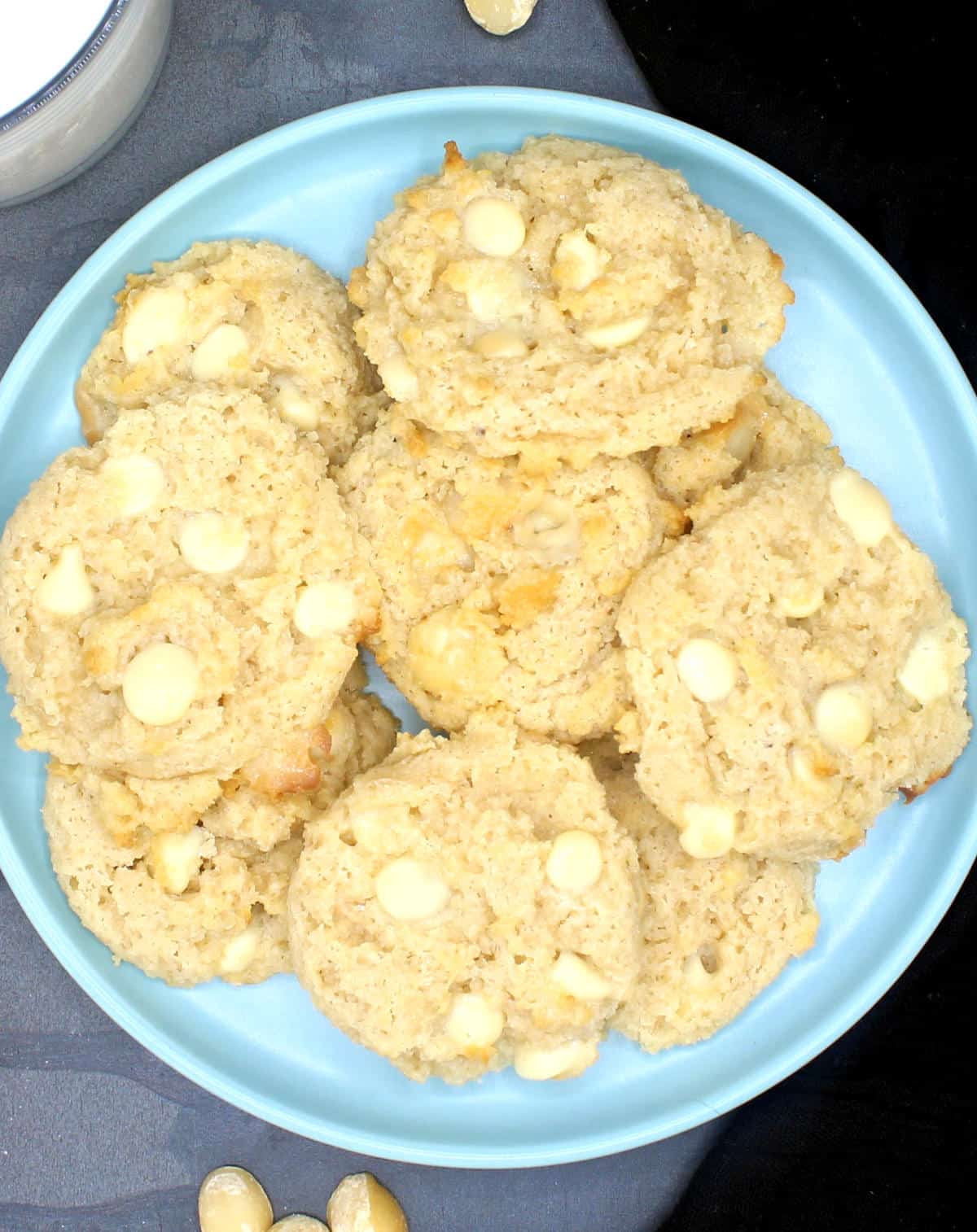 Vegan keto white chocolate macadamia nut cookies in blue plate with nuts scattered around.