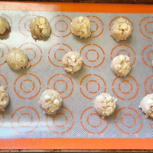 Cookie dough balls scooped out on silpat sheet in baking sheet.