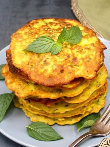 Stack of cucumber pancakes in gray plate with mint leaves.