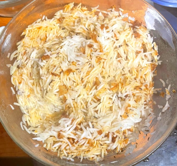 Rice mixed with fried onions and biryani masala in glass bowl.