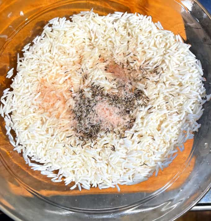Uncooked rice with shahi jeera and salt in glass bowl.