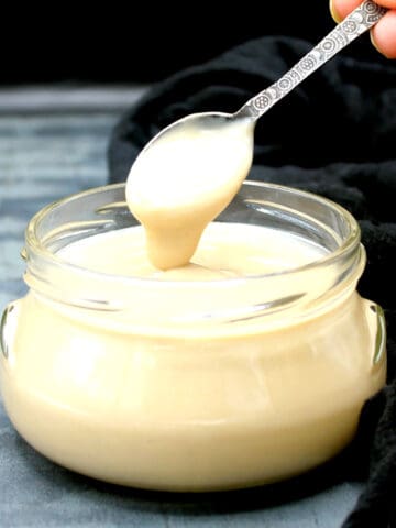 A glass jar with vegan condensed milk with a spoon.