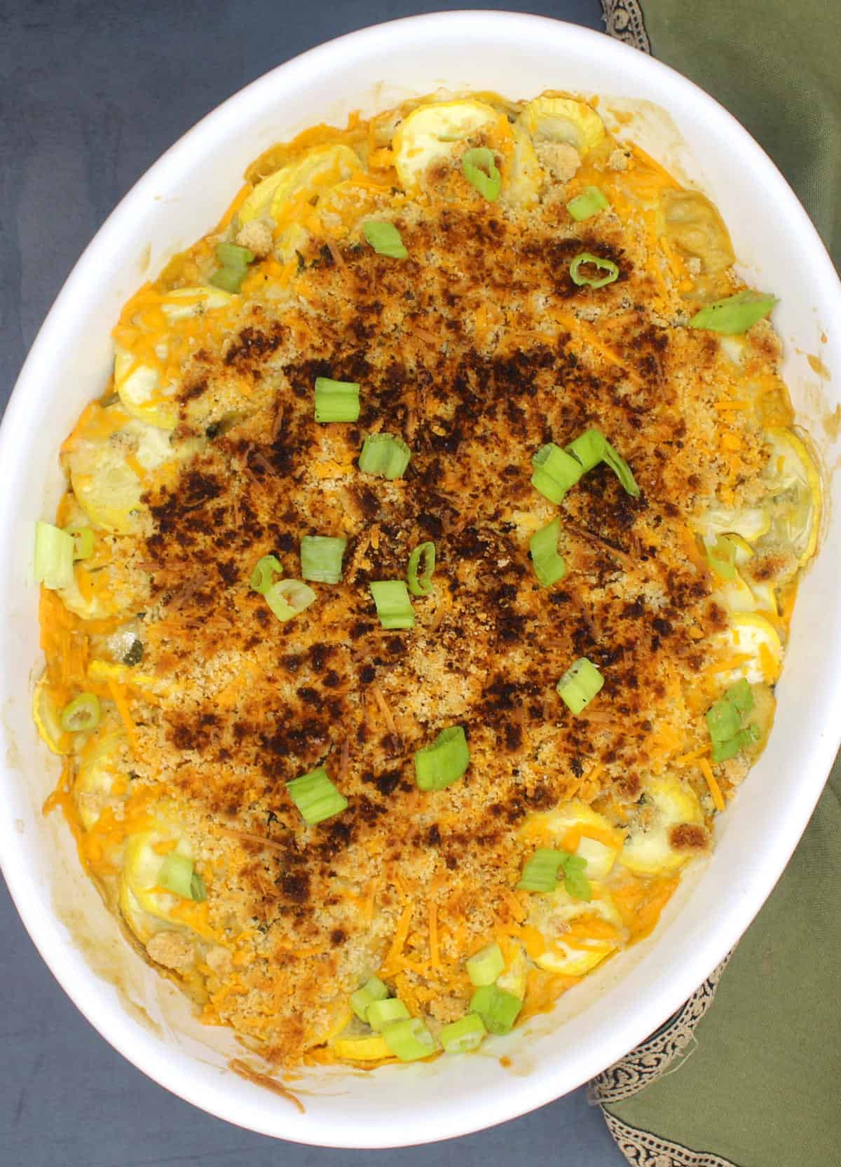 An oval baking dish with vegan squash casserole with green onions garnish.