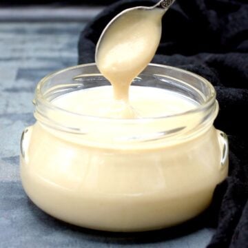 Vegan condensed milk being poured into glass jar with spoon.