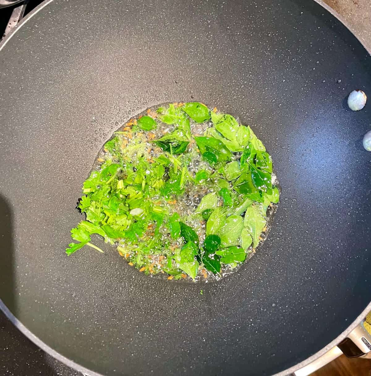 Curry leaves and cilantro frying in oil.