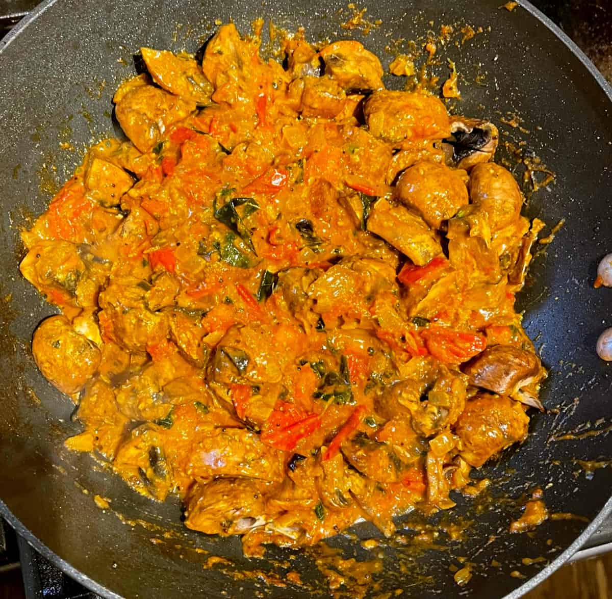 Mushrooms added to masala sauce in wok.