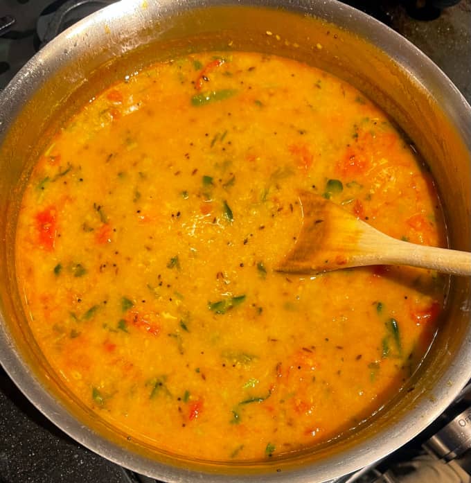 Cooked dal in steel saucepan with wooden ladle.