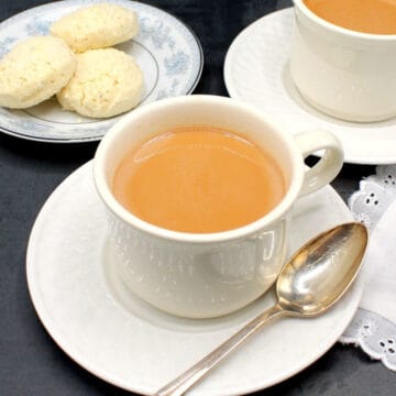 Masala chai tea in white cups with a side of cookies.
