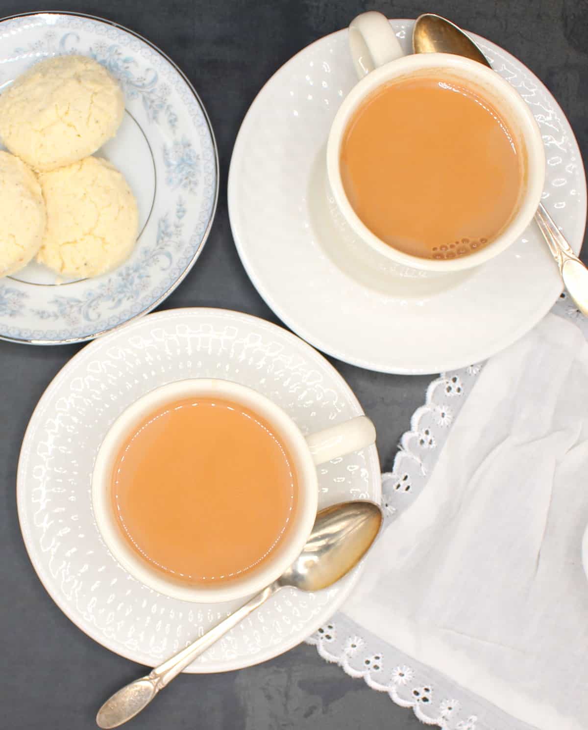 Masala chai in white cups and saucers with biscuits on the side.
