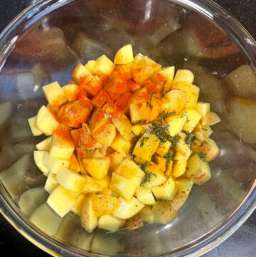 Seasonings added to cubed potatoes in bowl.