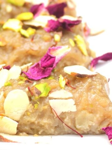 Vegan kalakand on white plate with rose petals, nuts and saffron.
